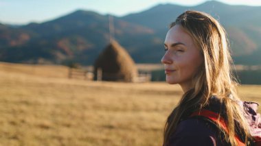 Turist kadın, Ukrayna 'nın Karpat Dağları' nda sonbahar günbatımının tadını çıkarıyor. Köyün kırsal kesimindeki sarı çim tarlasına bakan uzun saçlı beyaz kız. Seyahat, yürüyüş, özgürlük ve aktif yaşam tarzı