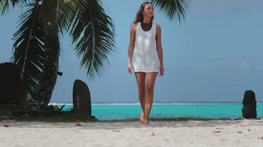 Beyaz kadın, egzotik yaz tatilinde. Beyaz elbiseli mutlu kız egzotik bir adada yürüyor. Beyaz kumsal, palmiye ağacı, turkuaz su. Yaz tatilinde açık hava seyahati. Tropik sahne