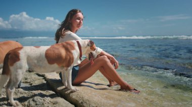 Kayalık sahilde oturan bir kadın köpekle kumsalda rahatlar. Sahilde birbirine sarılıp okyanus dalgalarını seyreden bir köpek. İnsanlar ve evcil hayvanlar hafta sonunun tadını çıkarırlar. Sakin sakin, güzel doğa.