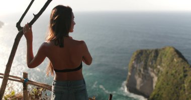 Nusa Penida Adası 'nı ziyaret etmek için turistik bir yer, Kelingking Gizli Nokta Sahili Endonezyası. Kafkasyalı güzel kadın rahatla ve okyanus dağlarının vahşi doğasının tadını çıkar. Yavaşça yakınlaştır