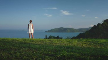 Genç bir kadın yemyeşil bir tepede duruyor, okyanusa ve Tayland adalarına bakıyor, dingin ve özgür hissediyor. Sahne, huzur ve gezginliğe ilham veriyor. Huzurlu bir kaçış için mükemmel.
