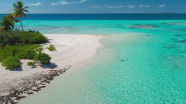 Güneşli bir günde, kristal berraklığında turkuaz suyla çevrili, uzak bir adada güneşlenen bir kadının hava görüntüsü.
