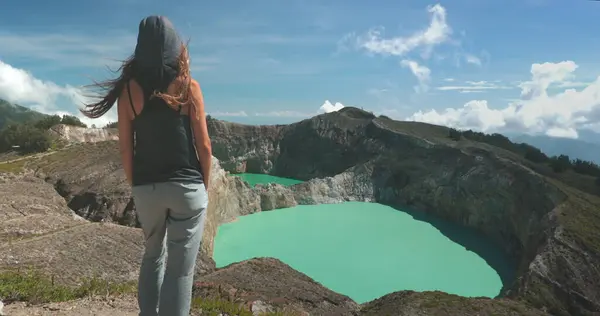 Bir kadın, Filipinler 'in arka planında bir volkanla, çarpıcı bir göle bakan bir dağın tepesinde duruyor..