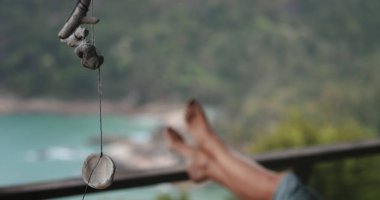 Rüzgarda sallanan deniz kabukları ve mercanlar. Arka planda çıplak ayaklı bir kadın, deniz kenarında rüzgarda sallanan bir ipe bağlanmış deniz kabuklarını kapatır. Rahatlama, sessizlik ve sükunet. Yavaş