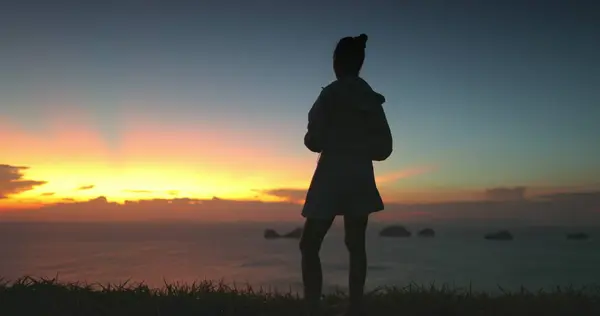 stock image A woman stands silhouetted against a breathtaking sunset over the ocean in a Thailand resort. The sky with vibrant hues of orange, yellow, and pink, creating a dramatic backdrop for this serene moment