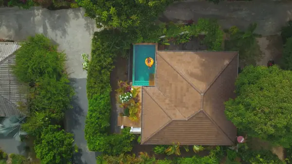 stock image Aerial view of a woman enjoying her vacation floating on a yellow inflatable ring in a swimming pool at a tropical luxury villa