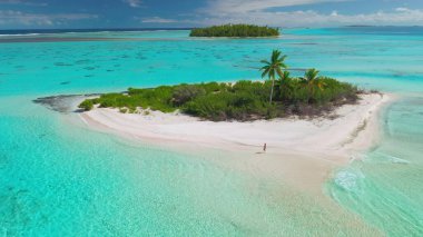 Maldivler 'deki bir turkuaz gölün ortasında, küçük ıssız bir adanın beyaz kumlu sahilinde yürüyen genç bir kadının hava görüntüsü..