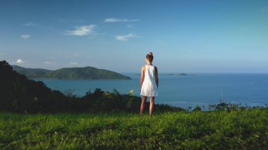 Kızların üzerindeki İHA uçuşu tropik bir adanın okyanusunda duruyor. Kadınlar, hava manzaralı egzotik manzaralardan hoşlanırlar. Beyaz elbiseli kız yeşil çimlerde, palmiye ağaçlarında ve arka planda mavi gökyüzünde rahatlıyor. Arka plan