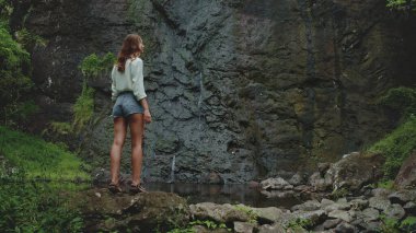 Doğada şelale manzarasının tadını çıkaran bir kadın, macera arayanlar için mükemmel. Açık havada keşif için sakin bir ortam.