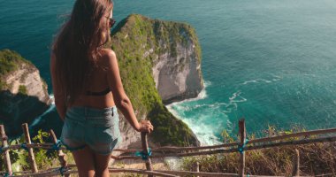 Endonezya 'daki Nusa Penida Adası' ndaki engin okyanusa bakan kayalık bir uçurumda duran bir kadın. Dalgalar sahile çarpar ve ufka bakar..