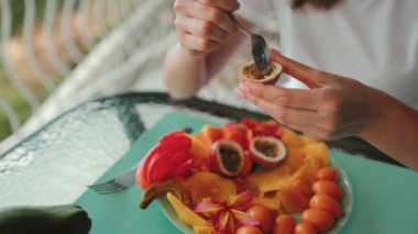 Tutku meyvesi hamurunu kepçeleyen bir kadın, bir tabak taze egzotik meyvenin tadını çıkararak vitaminler ve antioksidanlarla sağlıklı bir yaşam tarzını somutlaştırıyor.