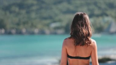 Genç bir kadın tenha bir plajda dinlendirici bir yürüyüşün tadını çıkarıyor. Turkuaz okyanusun güzelliğini ve bereketli tropikal çevresinin tadını çıkarıyor.