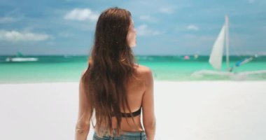 Kadın, kumlu Boracay Adaları Beyaz Sahili 'nde, okyanusta zarif bir şekilde yüzen yelkenliyi seyrediyor. Tropik doğa manzarası, turkuaz su ve mavi gökyüzü. Seyahat, turizm, tatil. Arka plan