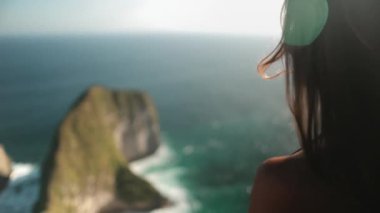 Genç bir kadın, Endonezya, Nusa Penida 'daki Kelingking plajında gün batımını izlerken uçurumun kenarında büyülenmiş bir şekilde duruyor.
