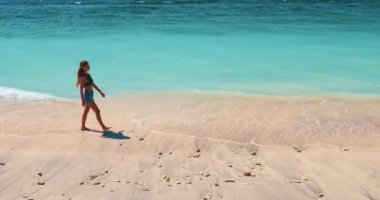 Beyaz kumsal ve turkuaz deniz suyu arka planı. Uzun saçlı, esmer, genç, çıplak ayaklı bir kadın tropik adada tatilin tadını çıkarıyor. Seyahat, turizm, tatil, aktif yaşam tarzı