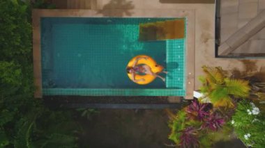 Tayland 'da kristal bir yüzme havuzunda sarı ördek üzerinde dinlenen bir kadının hava görüntüsü. Turkuaz su ve yemyeşil çevre huzurlu ve cennet gibi bir atmosfer yaratır..