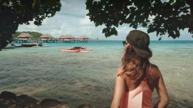 Genç bir kadın tropik bir cennette deniz aşırı bungalovların keyfini çıkarıyor. Turkuaz göl ve yemyeşil bitki örtüsü nefes kesici bir manzara yaratır.