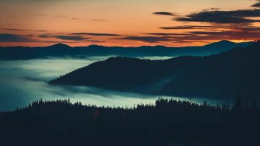Gün doğumu sisli denizi dağ sırasının üzerinden geçiyor. Zaman atlaması dağ siluetini çam ağacı orman havası manzaralı hale getirir. Vahşi doğa sisi manzarası. Turuncu renkli gökyüzünde dramatik kara bulutlar süzülür.