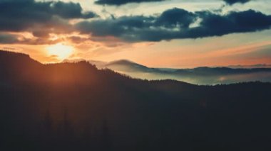 Alp dağlarında destansı sisli, renkli gün doğumu. Parlak gökyüzünde dramatik bulutlar akıyor, altın ışık huzmeleriyle dağ zirvesinde yükselen güneş ışığı. Güzel sabah doğası yaz manzarası. Zaman aşımı