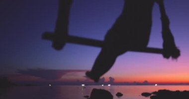 Salıncakta sallanan bir kadın, Tayland 'da sakin bir su kütlesiyle yüzleşirken yavaşça ileri geri sallanıyor..