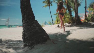 Beyaz kumsalda koşan bir kadın, palmiye ağaçları, tropik Borakay adası, Filipinler. Uzun saçlı, zayıf, beyaz tenli esmer gevşemiş, açık hava sporlarının tadını çıkarmış, yaz tatilinde seyahat etmiş. Yavaş çekim