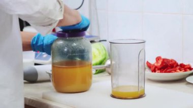 Profesyonel beyaz mutfakta aşçı blender bardağında bal ve portakal suyu ile tatlı sosis yapar. Yemek pişirmek, restoranın içindeki malzemeleri hazırlamak. Sağlıklı ve diyet gıda teslimatı konsepti. 4K atış