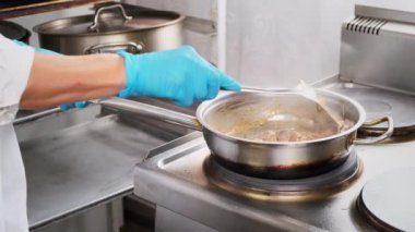 Kadın tavada et pişiriyor. Eldivenli şef, kremalı soğan soslu tavuk ciğeri pişiriyor. Yemek pişirin, profesyonel restoranda sağlık ve diyet gıda dağıtımı için malzemeler hazırlayın.