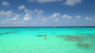 Güneşli bir günde mavi bulutların altında kristal turkuaz deniz suyunda yüzen kadın. Turist kız, yaz tatilinde rahatlar ve açık hava yolculuğunun tadını çıkarır. Hava görüntüsü drone görüntüleri