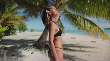 Güzel bir kadın tropik plajda dinlenir. Esmer, beyaz saçlı, çiçekli bir kadın. Fransız Polinezyası 'nın egzotik Tikehau adasında güneşli bir günün tadını çıkarıyor. Palmiye ağacı, beyaz kum. Yavaş çekim