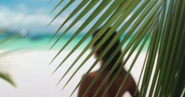 Kadın yaklaşır palmiye yaprağının arkasında gevşer rüzgarda güneş ışığıyla sallanır. Boracay tropik ada plajındaki esmer kız portresi. Yaz tatili kavramı. Ağır çekimde yakınlaştır