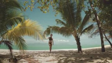 Tayland 'da palmiye ağaçlarının altında beyaz kumsalda yürüyen bir kadın. Turkuaz su ve parlak mavi gökyüzü tropikal cennet arka planı. Yaz tatilinde açık hava seyahati. Eski tonlama
