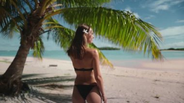 Kadın Polinezya 'daki tropik ada plajında dinleniyor. Palmiye yaprağı altında bikinili zayıf esmer kız egzotik deniz manzarasının tadını çıkarıyor. Yaz tatilinde açık hava seyahati. Yavaş çekim