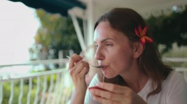 Masada oturan bir kadın egzotik meyve yemekle meşgul. Yemeğine odaklanmış görünüyor, çatal bıçak tutuyor ve ağzına yemek getiriyor..