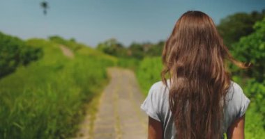 Uzun saçlı kadın Campuhan Tepesi Yolu 'nda yürüyor. Ubud, Bali adasında ziyaret etmek için turistik bir yer. Yeşil alan, mavi gökyüzü. Yaz tatilinde açık hava seyahati. Arka planı kapat, yavaş çekim