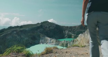 Kelimutu Mavi Krateri 'ne doğru yürüyen kadın turist dağ kıyısında. Uzun saçlı, uzun saçlı, rüzgarda savrulan saçları olan bir kız. Seyahat, turizm, tatil, yürüyüş, dinlenme. Yavaş çekim 4K