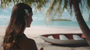 Fransız Polinezya egzotik adalarına seyahat edin. Turist kadın hindistan cevizi ağacının altındaki deniz manzarasının tadını çıkarıyor. Çiçekli beyaz kadın dışarıda dinleniyor, yaz tatili. Yavaş çekim