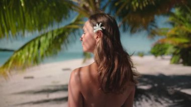 Kadınlar cennette, egzotik ada kumsalında rahatlarlar. Saçında çiçek olan Kafkas dişisi palmiye yaprağı altında tropik ada manzarasının tadını çıkarıyor. Açık hava yaşam tarzı yaz tatili tatili. Yavaş çekim