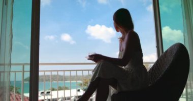 Beyaz kadın silueti balkonda kahve içiyor ve okyanus manzarasının tadını çıkarıyor. Kadın Phuket, Tayland deniz doğasında dinleniyor. Tropik adaya yaz tatili için hayat tarzı seyahati. Otelde mükemmel bir sabah.