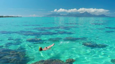 Genç kadın kristal berrak turkuaz suda şnorkelle yüzüyor. Arka planda Moorea adası olan güzel tropikal gölde yaz tatilinin tadını çıkarıyor.