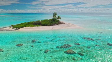 Tropikal bir adada el değmemiş beyaz bir kumsal boyunca yürüyen genç bir kadının hava manzarası kristal berrak turkuaz su ve yemyeşil palmiye ağaçları ile çevrili.
