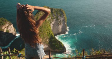 Endonezya 'daki Nusa Penida Adası' ndaki engin okyanusa bakan bir uçurumun tepesinde duran bir kadın. Aşağıdaki nefes kesen manzarayı izlerken sahne onu derin derin yakalar..