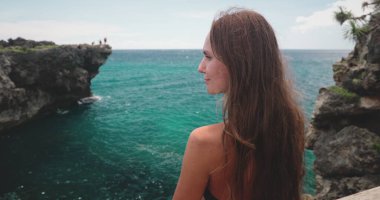 Romantik kız kaya uçurumu ve turnuva suyuyla deniz manzarasını sever. Uzun saçlı, ince esmer, genç bir kadın. Seyahat, tatil, yürüyüş, özgürlük. Endonezya, Vahşi Sumba Adası, Weekurri Gölü