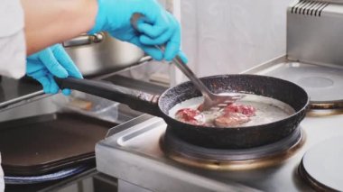 Lokanta mutfağında aşçı sıcak tavada ızgara et yapıyor. Mavi eldivenli profesyonel aşçı karaciğeri demir mutfak spatulasıyla karıştırır. Yemek pişirme, sağlık ve diyet gıda teslimatı için malzeme hazırlama