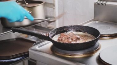 Sıcak tavada ızgara tavuk ciğeri yakın plan. Mavi eldivenli profesyonel aşçı demir mutfak spatulasıyla eti karıştırıp çıkarıyor. Yemek pişirme, sağlık ve diyet gıda teslimatı için malzeme hazırlama