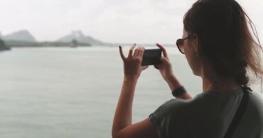 Kadın cep telefonuyla deniz manzarasının fotoğrafını çekiyor. Arkaya bakan turist kız, Tayland 'daki Koh Phangan adasına giden feribotta deniz manzarasının tadını çıkarıyor. Seyahat, turizm, tatil, yavaş çekim