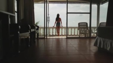 Genç ve güzel bir kadın plaj tatilinin tadını çıkarıyor. Bikinili beyaz kız, villa terasında rahatlayıp vahşi doğa okyanus manzarası seyrediyor. Tayland 'daki tropikal adalarda tatil. Arkadan bak. Yavaş çekim