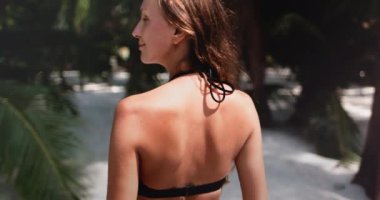 Genç kadın tatilinin tadını çıkarıyor, Tayland 'da beyaz bir kumsalda yürüyor. Okyanusa doğru yürürken saçları rüzgarda uçuşuyor.