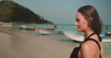 Arka planda geleneksel Tayland tekneleriyle Bottle Beach, Koh Phangan 'ın kumlu sahillerinde bir kadın duruyor. Kız sakin havanın ve sakin öğleden sonranın yumuşak esintisinin tadını çıkarıyor..