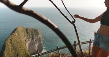 Genç kadın, turkuaz okyanusun ve ikonik kelingking plajının büyüleyici panoramik manzarasını manzaralı bir uçurum manzarasından alıyor.