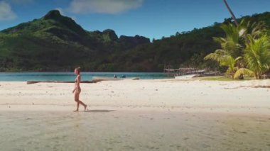 Kadın tropik bir plajda yürüyor, palmiye ağaçları, temiz su ve mavi gökyüzü, huzurlu bir tatil yeri yaratıyor.